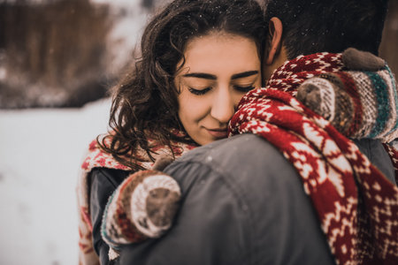 young man and woman stand kissing and hugging. bride and groom in love couple in knitted scarf and mittens in winter with snow and snowflakes. wedding dress. mexican peopleの写真素材