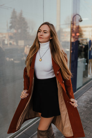 young blonde woman in autumn clothes walks on street background shop windows. Street style Fashion 2021 Winter Spring Terracotta Coat Woolen Cashmere Suede Over Knee Boots White Golfの写真素材