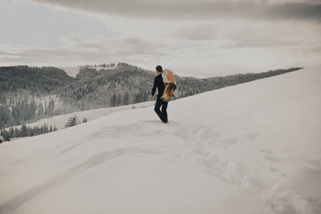 Groom took his bride on shoulder and carried her away through the snow against the backdrop of hilly mountains dotted with pine and Christmas trees.の写真素材