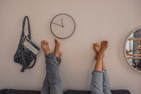 People raised feet up laid on the wall.A man and a woman bare feet are lying on the bed.on light beige wall hanging bag with a magazine beautiful watch and mirrorの写真素材