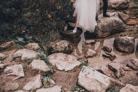 a legs of couple newlyweds In wedding clothes. a transparent water and gray stones. bride in a white long dress and a slim man groomの写真素材