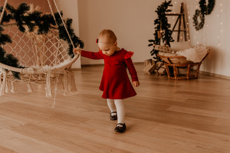 little girl in red dress runs apartment style light minimalism. child stands at white wall with garlands Christmas tree with wrapped gifts. Christmas.New Year interior.Valentine Day celebrationの写真素材
