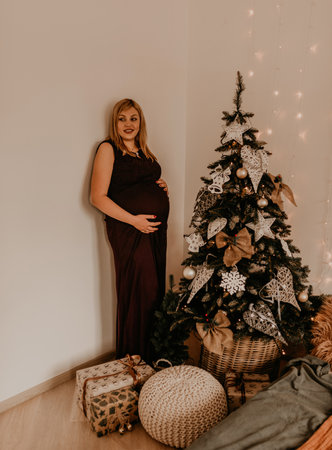 pregnant woman in long black dress near the Christmas decorated tree. Christmas morning. New Year's interior. Valentine's day celebrationの写真素材