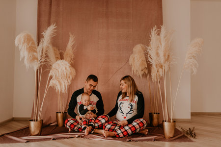 family photo in studio on beige background with flowers dry reeds. clothes for baby child.pregnant woman in pajamas.Christmas morning.New Year interior.Valentine's day celebrationの写真素材