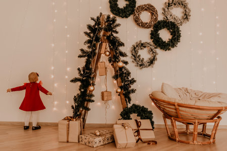 little girl in red dress runs apartment style light minimalism. child stands at white wall with garlands Christmas tree with wrapped gifts. Christmas.New Year interior.Valentine Day celebrationの写真素材