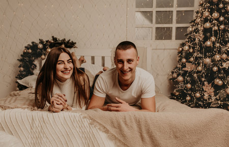 couple man and woman lie on bed bedroom near christmas tree.decorated house for New Year.Christmas morning. apartment interior. Valentine's day celebrationの写真素材