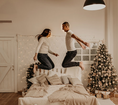 young couple man and woman jumping on bed in bedroom treedecorated house for New Year. Christmas morning. apartment interior. Valentine day celebrationの写真素材