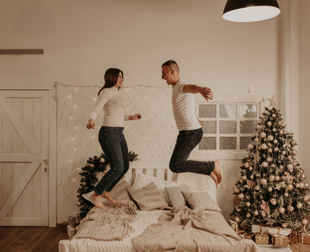young couple man and woman jumping on bed in bedroom treedecorated house for New Year. Christmas morning. apartment interior. Valentine day celebrationの写真素材