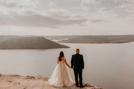 loving couple wedding newlyweds in white dress and suit walk in summer on mountain above river. sunset and sunrise. man and woman on rocks above cliffの写真素材