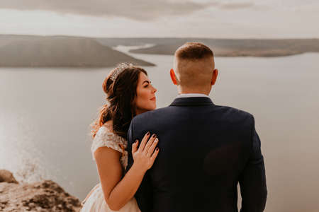 loving couple wedding newlyweds in white dress and suit walk in summer on mountain above river. sunset and sunrise. man and woman on rocks above cliffの写真素材