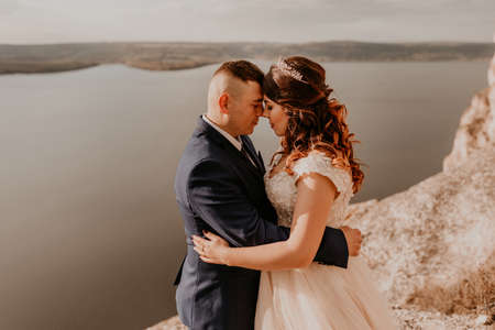 loving couple wedding newlyweds in white dress and suit walk in summer on mountain above river. sunset and sunrise. man and woman on rocks above cliffの写真素材