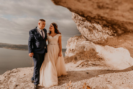 loving couple wedding newlyweds in white dress and suit walk in summer on mountain above river. sunset and sunrise. man and woman on rocks above cliffの写真素材