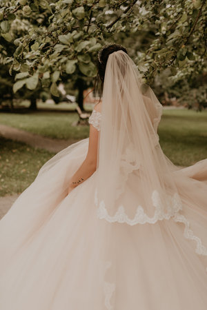 dark-haired European Caucasian young woman bride in white wedding dress with long veil and tiara on head spinning whirls dancing posing moving at nature on background greenery. Valentine love coupleの写真素材