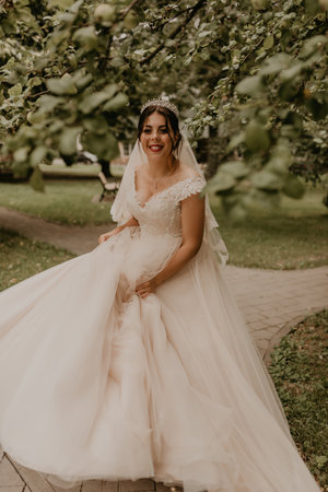 dark-haired European Caucasian young woman bride in white wedding dress with long veil and tiara on head spinning whirls dancing posing moving at nature on background greenery. Valentine love coupleの写真素材