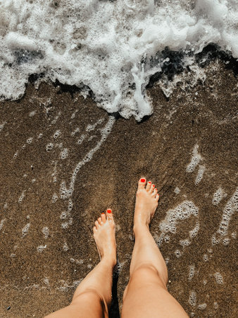 Woman legs barefoot at sea foam waves on sand beach summer day. top view above women feet. Ocean...