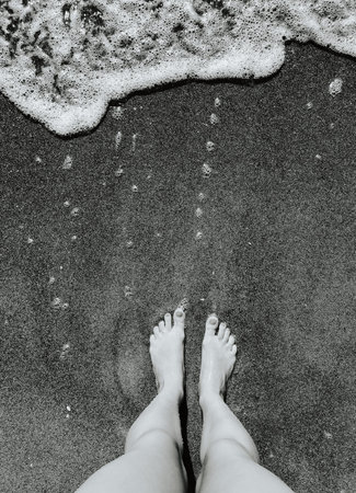 Woman legs barefoot at sea foam waves on sand beach summer day. top view above women feet. Ocean...