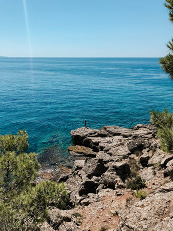 Old man hobby fishing angling standing on big rock stone. senior pensioner catches fish spinning. Top view Montenegro Sutomore stones beach turquoise Adriatic sea water mountains. Summer backgroundの写真素材