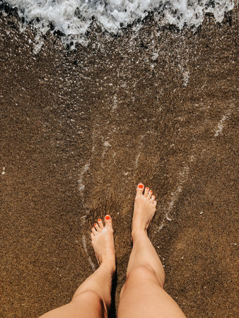 Woman legs barefoot at sea foam waves on sand beach summer day. top view above women feet. Ocean clear water seafoam. girl on beach Summer background nature concept holiday vacation. natural wallpaperの写真素材