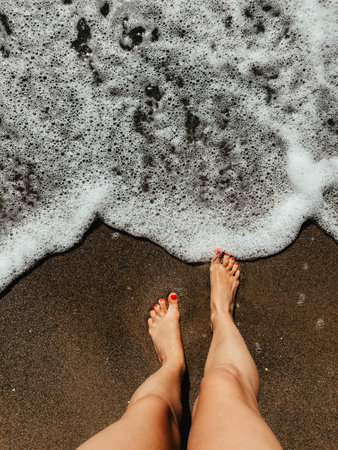 Woman legs barefoot at sea foam waves on sand beach summer day. top view above women feet. Ocean clear water seafoam. girl on beach Summer background nature concept holiday vacation. natural wallpaperの写真素材