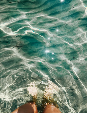 Woman legs barefoot at sea waves stones beach summer. top view above women feet. Ocean clear water...
