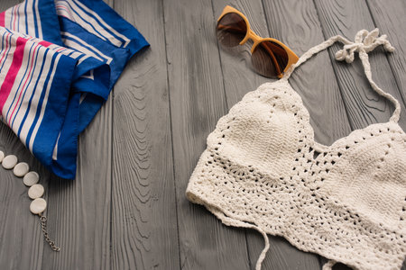 white knitted top woman trending two-piece swimsuit beach swimwear fashion sunglasses. Summer background template mockup space pattern composition sample text. Top view above grey wooden background.の写真素材