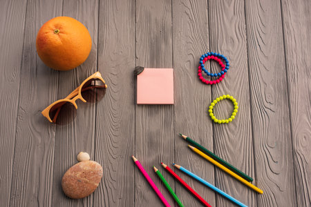 artist pencils for inscription. accessories sunscreen spf care. sunglasses bracelets orange fruit pebbles. Summer background template mockup space colorful composition text. Top view wooden backgroundの写真素材