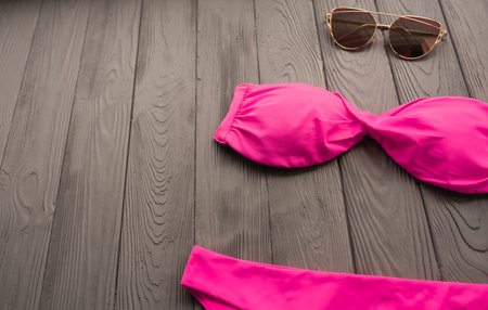 woman trending two-piece swimsuit beach pink swimwear fashion sunglasses. Summer background template mockup copy free space colorful composition sample text. Top view above grey wooden background.の写真素材