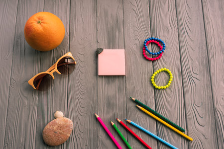 artist pencils for inscription. accessories sunscreen spf care. sunglasses bracelets orange fruit pebbles. Summer background template mockup space colorful composition text. Top view wooden backgroundの写真素材