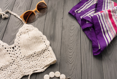 white knitted top woman trending two-piece swimsuit beach swimwear fashion sunglasses. Summer background template mockup space pattern composition sample text. Top view above grey wooden background.の写真素材