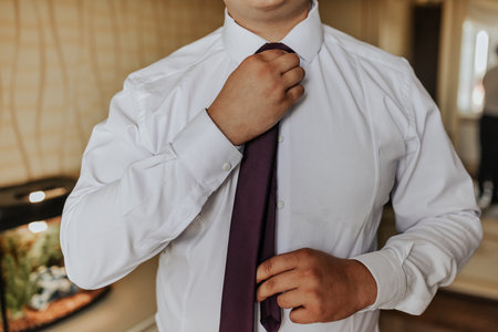 an adult man in a white strict shirt straightens his tie with his hands at homeの写真素材