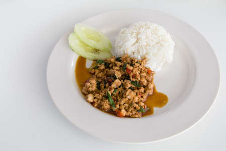 Thai Basil Chicken with rice (Pad Krapow) on white plate with cucumberの写真素材