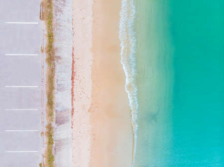 Aerial view of beach and blue sea with waves reaching shore along side with parking lotの写真素材