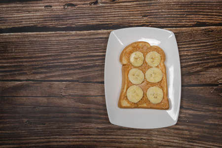 Bread spreading with peanut butter and banana on white plate. on wooden board. top viewの写真素材