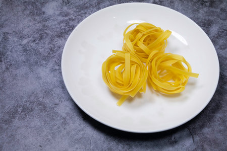 Raw Tagliatelle on white plate on concrete background
