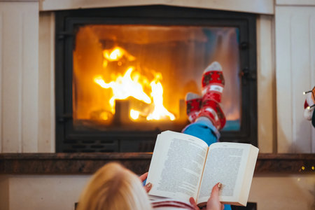 Mother and daughter reading a book in front of the fireplace at home