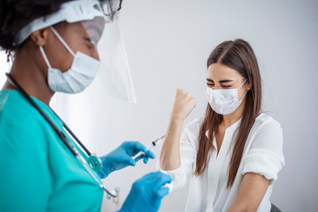 Female doctor in protective mask holding syringe with coronavirus vaccine