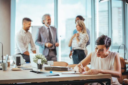 Young businesswoman writing on paper while her colleagues working in the backgroundの写真素材