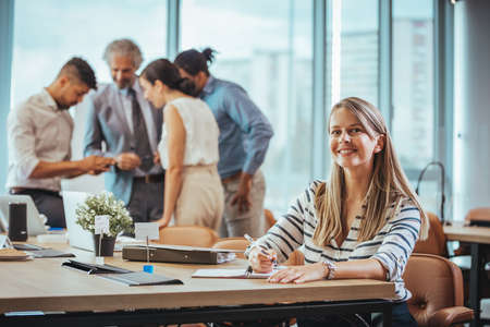 Happy businesswoman working in modern office with colleagues in the background.の写真素材