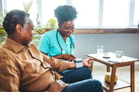 African american nurse checking blood pressure of senior man at nursing homeの写真素材