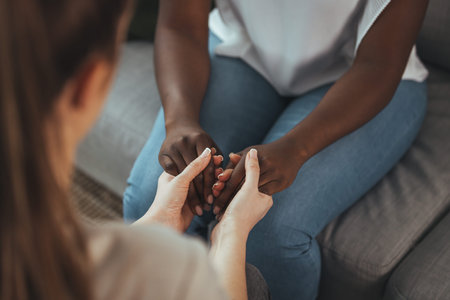 Close-up of a young woman holding her boyfriend's hand while sitting on the couch at home