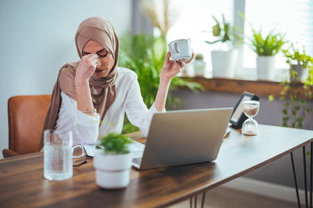 Portrait of muslim businesswoman in hijab using laptop and drinking coffee in officeの写真素材
