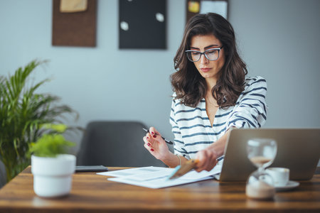 Young businesswoman working on laptop computer at office desk. Businesswoman in eyeglasses sitting...