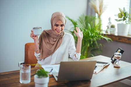 Beautiful young muslim businesswoman working with laptop and drinking coffeeの写真素材