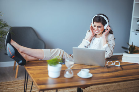Smiling woman in headphones listening to music and using laptop at homeの写真素材
