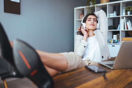 businesswoman listening to music with headphones while lying on sofa at homeの写真素材