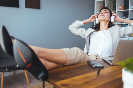 cheerful businesswoman in headphones listening to music while sitting at workplace