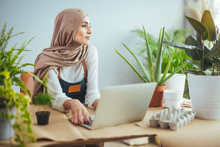 Portrait of young muslim businesswoman in hijab using laptop while sitting in modern officeの写真素材