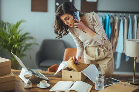Young business woman talking on the phone while packing a parcel in her officeの写真素材