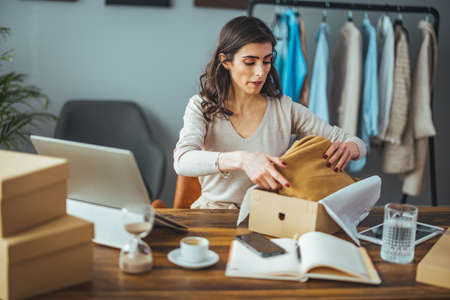 Young woman packing a parcel in her home office. Online shopping and delivery concept.の写真素材