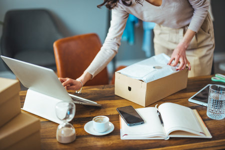 Cropped shot of young businesswoman using laptop while packing box into office